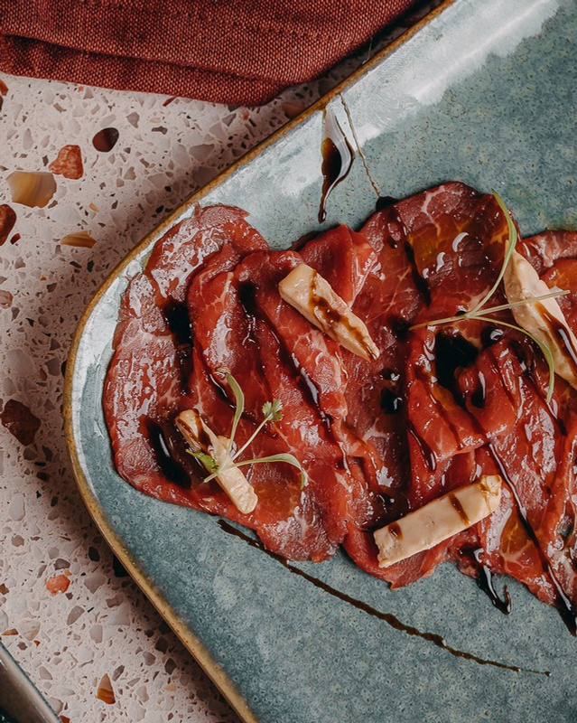 Beef carpaccio fanned across a stone plate with a balsamic drizzle.