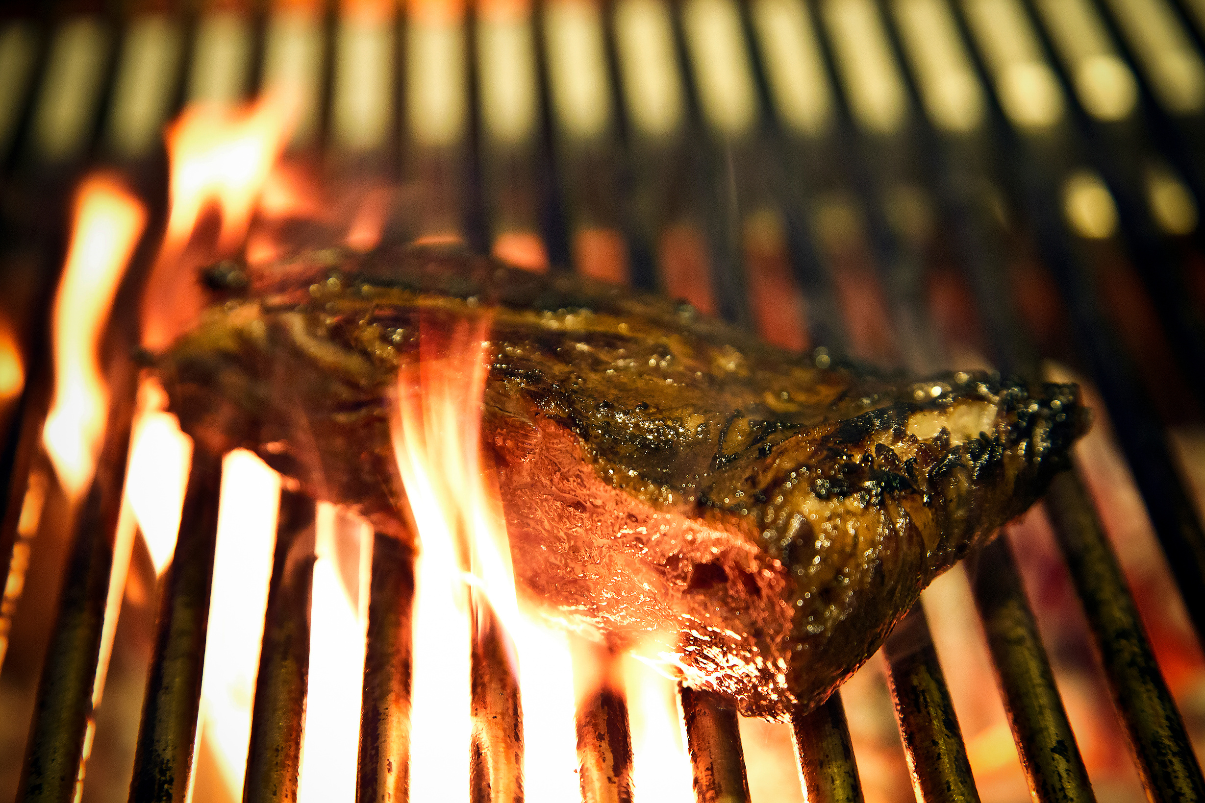 A cut of beef searing over open flame on the grill.