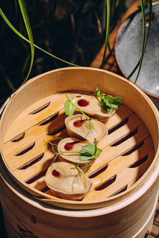 Wagyu gyoza in a bamboo steamer, finished with herbs.