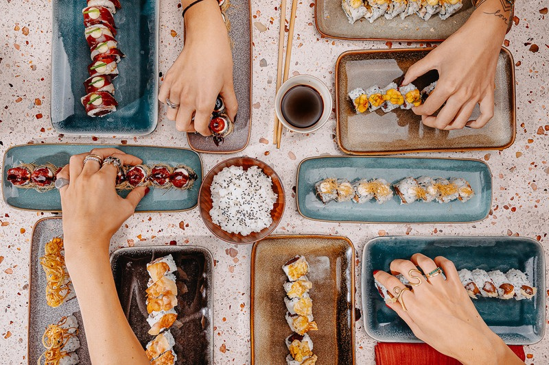 A table of Cantera beef rolls and beef sashimi seen from above, hands reaching in with chopsticks.