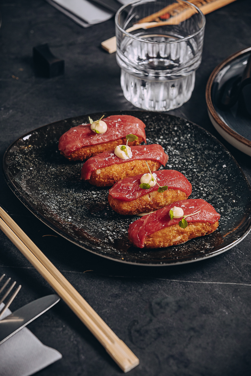Beef nigiri on a dark plate, the cut seared at the edge and pressed over rice.