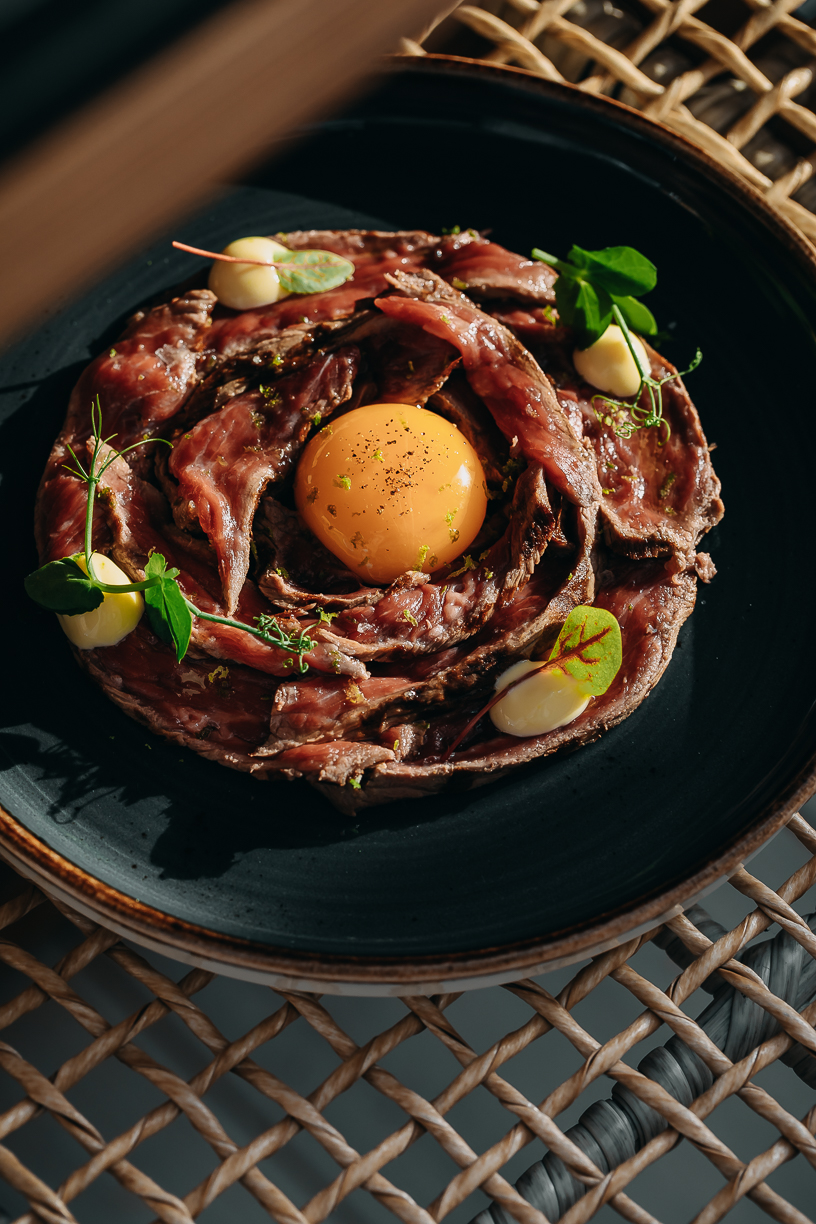 Hand-cut beef tartare ringed on a dark plate with a whole egg yolk at its centre.