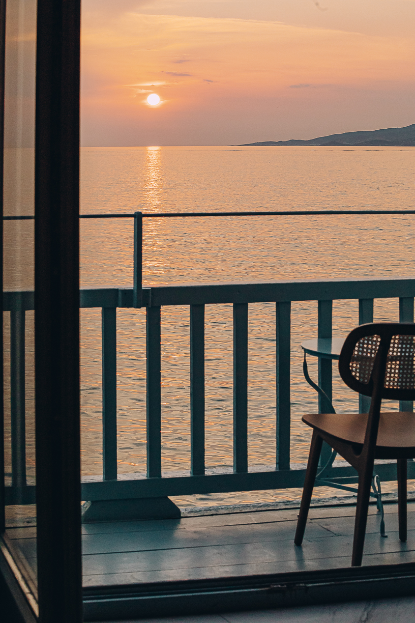 The sun on the horizon seen from a table at the balcony rail, the sea flat and gold beneath it.