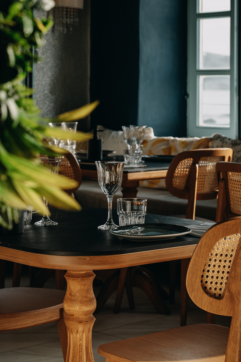 The dining room laid for service, cane chairs and dark tables against the sea windows.