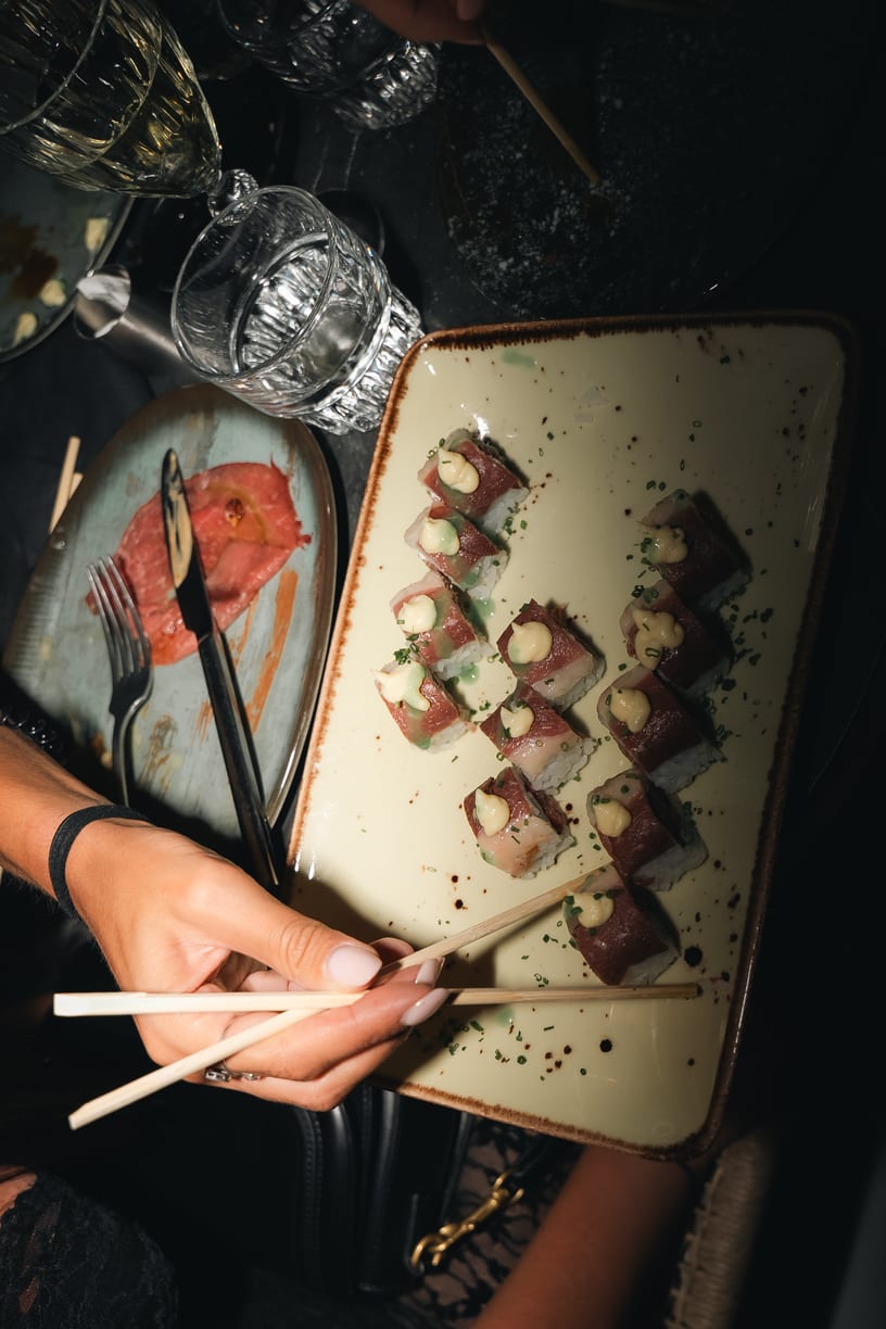 A platter of beef sushi and chopsticks between the glasses.