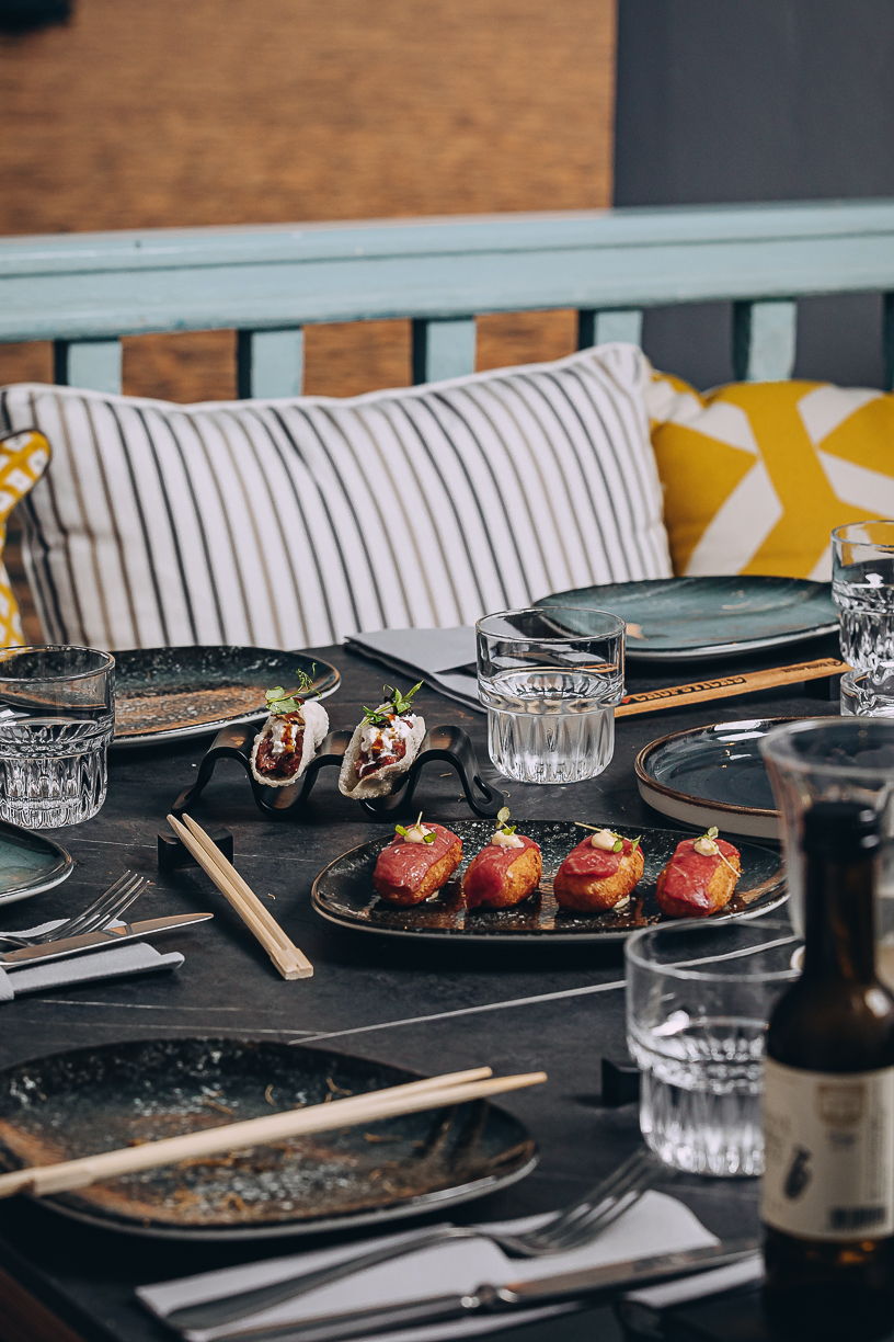 A table laid against the striped cushions of the window seat, glasses catching the last light.
